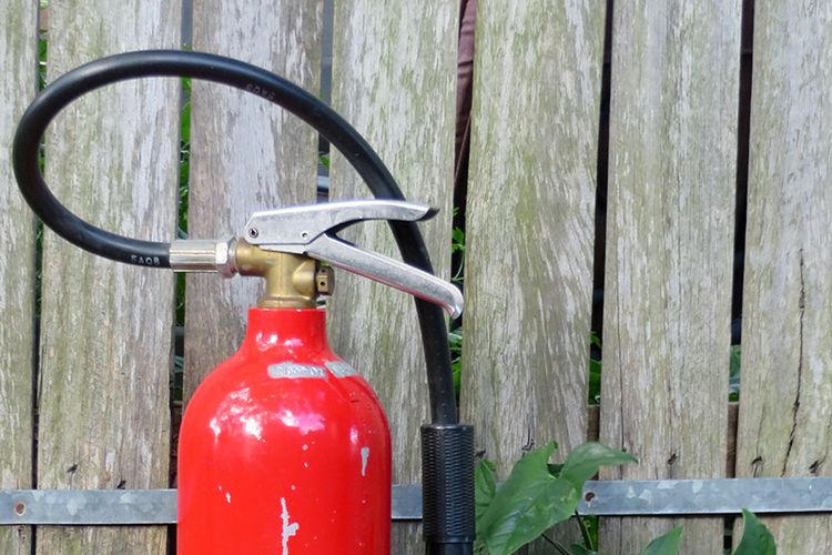 A red fire extinguisher with its hose and handle standing against a weathered fence