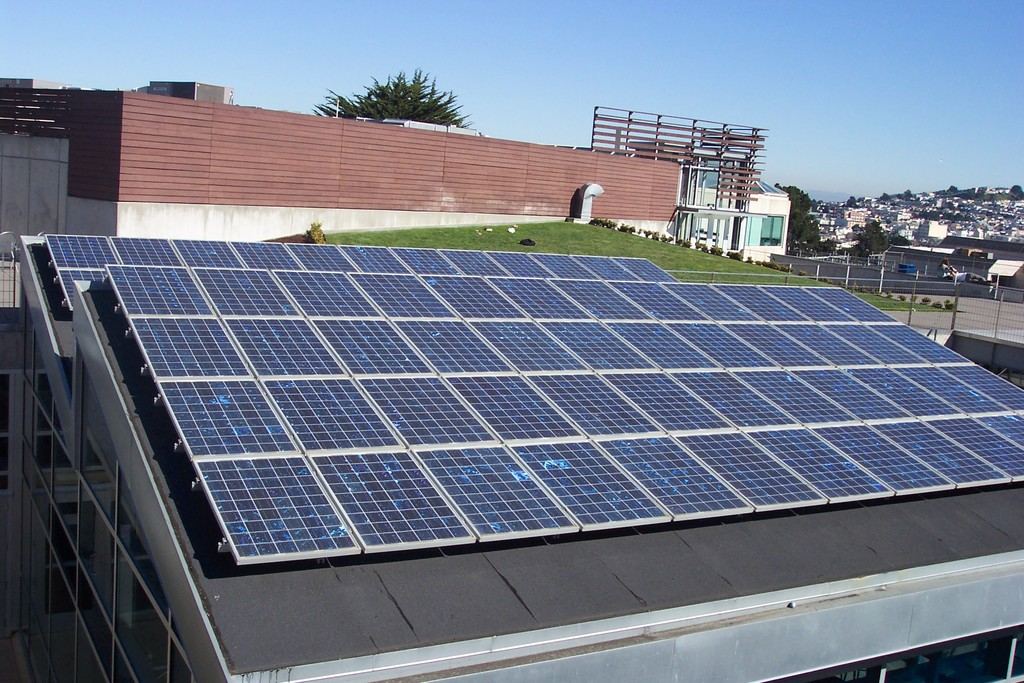 Rows of solar panels mounted across a rooftop under a clear blue sky
